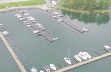 Aerofoto Baggö Marina jahisadamast, kus paadid on sildunud Top Marine toodetud ujuvkai külge, vaiksel veepinnal, ümbritsetuna metsast ja kivimuulidest.